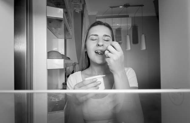 Schwarz-Weiß-Bild aus dem Kühlschrank einer jungen Frau, die nachts Joghurt isst