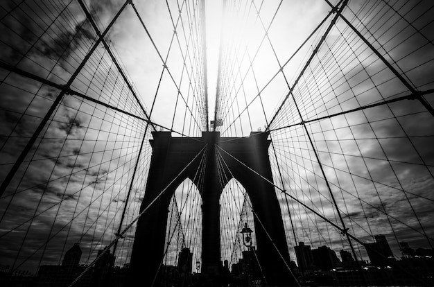 Schwarz-Weiß-Bild der Brooklyn-Brücken-Silhouette mit einem dramatischen Himmel und Sonnenstrahlen. New York City. USA.