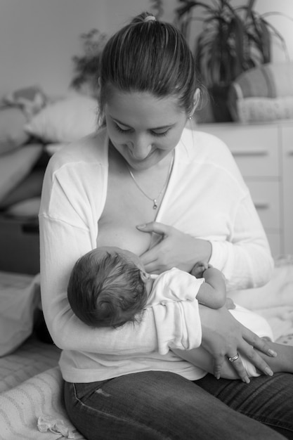 Schwarz-Weiß-Bild der jungen Mutter, die Baby mit Milch aus der Flasche füttert