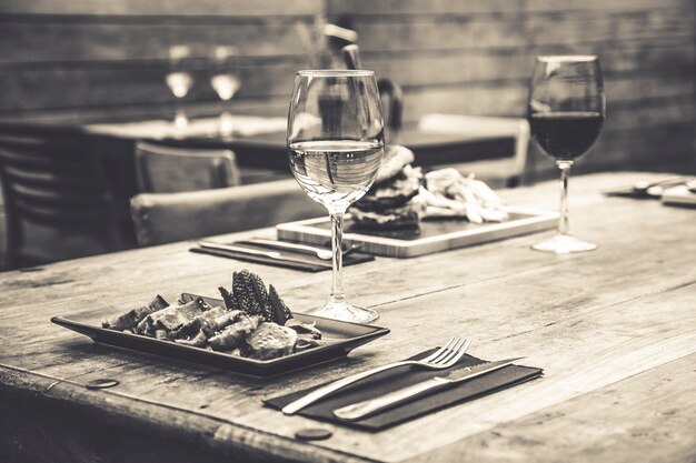 Schwarz-Weiß-Bild der traditionellen Restaurantatmosphäre mit Thunfisch-Tataki und Burger mit Pommes im Hintergrund auf rustikalem Holztisch und Glas Weißwein