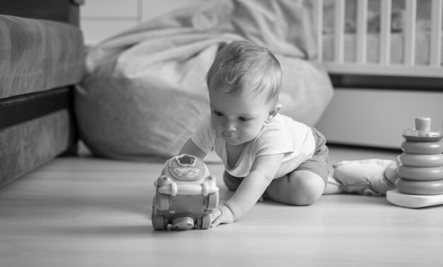 Schwarz-Weiß-Bild eines Jungen, der auf dem Boden krabbelt und nach Spielzeugauto greift