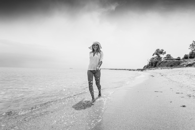 Schwarz-Weiß-Foto einer fröhlichen Frau, die am Sandstrand spazieren geht