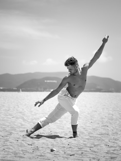 Schwarz-Weiß-Foto eines männlichen Tänzers, der am Strand posiert