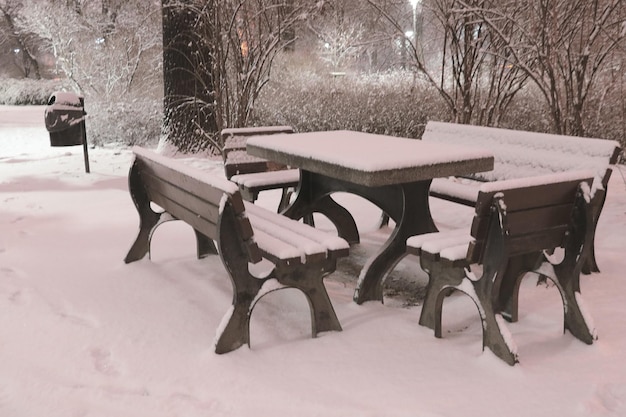 Schwarz-Weiß-Foto Verschneite Bänke und ein Tisch im Park am Abend