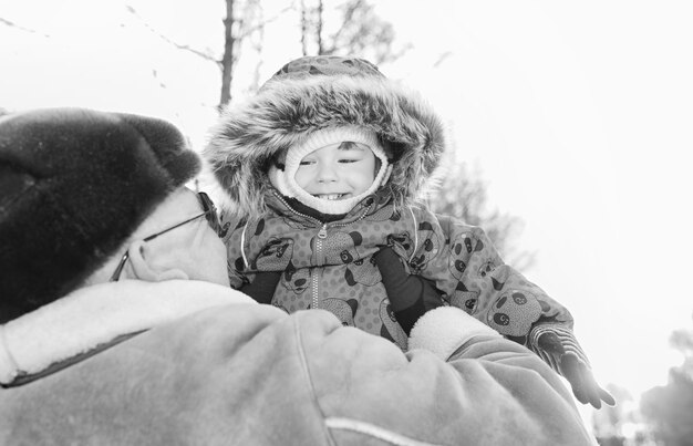 Schwarz-Weiß-Foto von Eltern, die Kind im Winterpark an den Händen halten