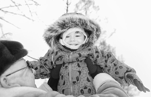 Schwarz-Weiß-Foto von Eltern, die Kind im Winterpark an den Händen halten