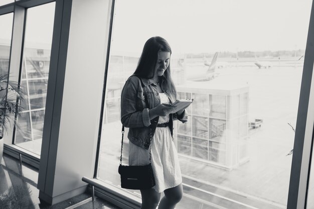 Schwarz-Weiß-Porträt der jungen Frau mit digitalem Tablet am Flughafen