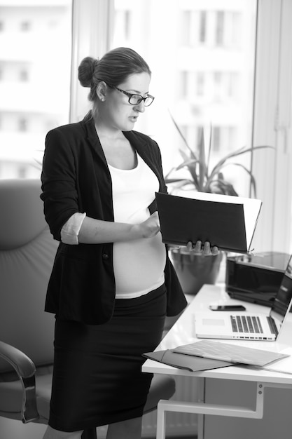 Schwarz-Weiß-Porträt einer Geschäftsfrau, die ein Baby erwartet, das im Büro arbeitet