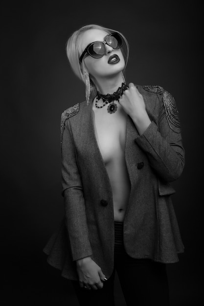 Schwarz-Weiß-Studioporträt einer sexy blonden Frau trägt eine Sonnenbrille und eine Jacke auf einem nackten Körper