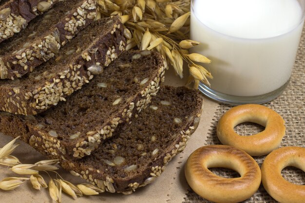 Schwarzbrot mit Sesam und Sonnenblumenkernen, Hafer, Weizenähren, ein Glas Milch