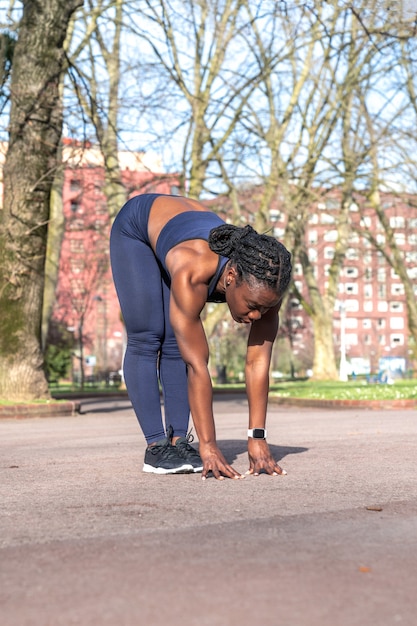 Schwarze Afrikanerin, die sich aufwärmt und Rücken- und Beinstrecken bückt, um an einem sonnigen Tag in einem öffentlichen Straßenpark Sport zu treiben?
