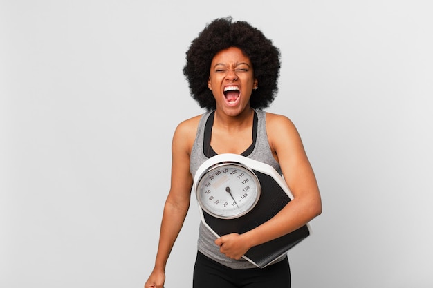 Schwarze Afro-Fitnessfrau mit Waage oder Waage