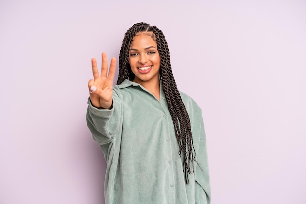 Schwarze Afro-Frau, die lächelt und freundlich aussieht und die Nummer drei oder drei zeigt, wobei die Hand nach unten zählt