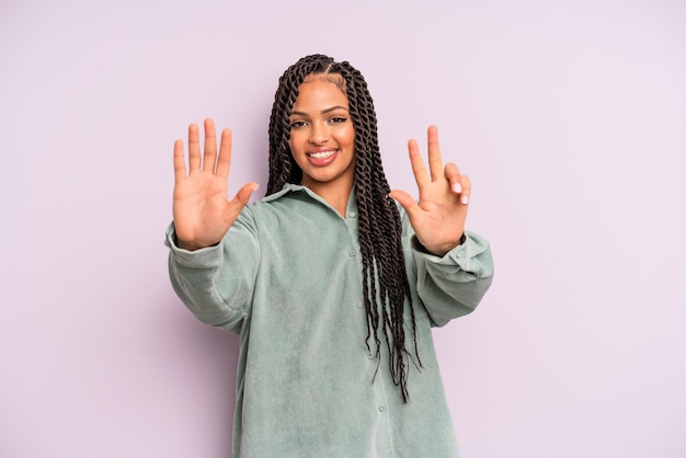 Schwarze Afro-Frau, die lächelt und freundlich aussieht und Nummer acht oder acht zeigt, wobei die Hand nach unten zählt