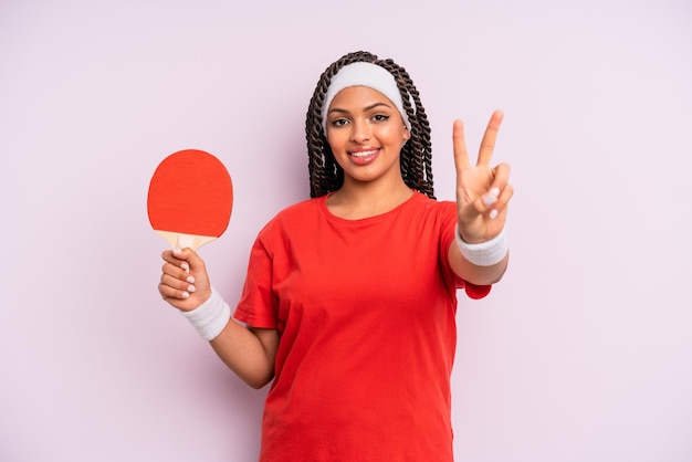 schwarze afro-frau, die lächelt und glücklich aussieht und sieg oder frieden gestikuliert. Ping-Pong-Konzept