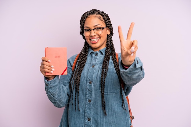 Schwarze Afro-Frau, die lächelt und glücklich aussieht und Sieg oder Frieden gestikuliert, Studentenkalender oder Tagesordnungskonzept