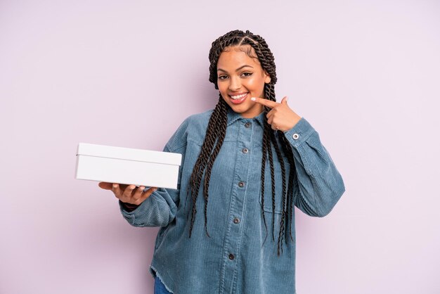 schwarze afro-frau, die selbstbewusst lächelt und auf ihr breites lächeln zeigt. Pakete-Box-Konzept