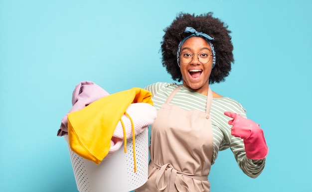Schwarze Afro-Frau, die sich glücklich, überrascht und stolz fühlt und mit einem aufgeregten, erstaunten Blick auf sich selbst zeigt. Hauswirtschaftskonzept .. Haushaltskonzept