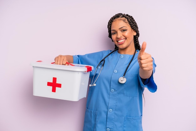 Schwarze afro-frau, die stolz ist und positiv mit den daumen lächelt. Konzept für Krankenschwester und Erste-Hilfe-Kit