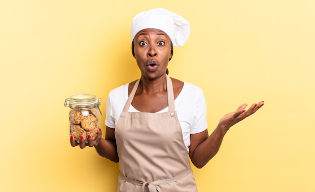 schwarze afro kochfrau mit offenem mund und erstaunt, schockiert und erstaunt über eine unglaubliche überraschung. Cookies-Konzept