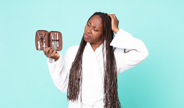 Schwarze afroamerikanische erwachsene Frau, die Bademantel trägt und eine Make-up-Tasche mit Nains-Tools hält