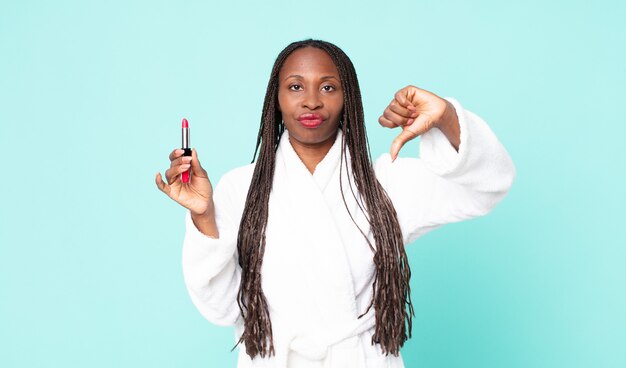 Schwarze afroamerikanische erwachsene Frau, die Bademantel trägt und einen Lippenstift hält?