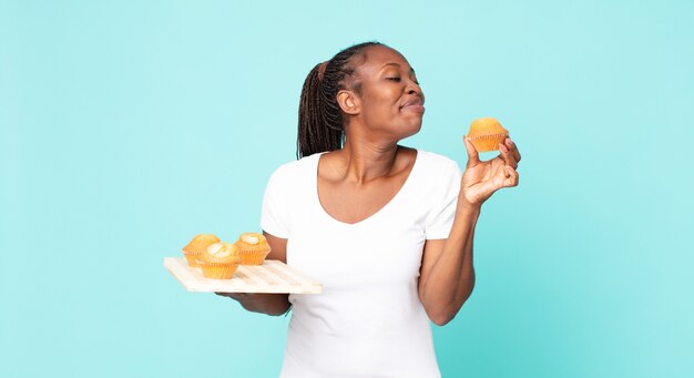 schwarze afroamerikanische erwachsene frau, die ein muffinsblech hält