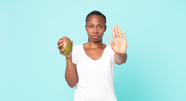 Schwarze afroamerikanische erwachsene Frau, die eine Mangofrucht hält