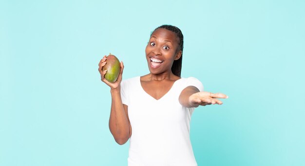 Schwarze afroamerikanische erwachsene Frau, die eine Mangofrucht hält