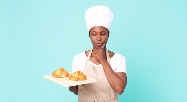 Schwarze afroamerikanische erwachsene Kochfrau, die ein Tablett mit Croissants hält