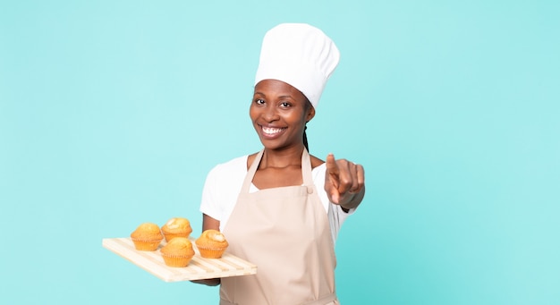 Schwarze afroamerikanische erwachsene Kochfrau mit einem Muffins-Tablett