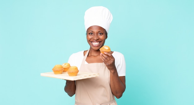 Schwarze afroamerikanische erwachsene Kochfrau mit einem Muffins-Tablett