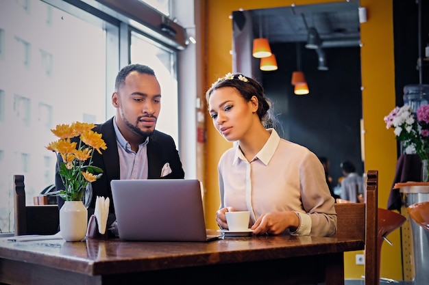 Schwarze afroamerikanische Geschäftsmänner und -frauen trinken Kaffee und benutzen einen Laptop in einem Restaurant.