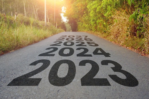 Schwarze Asphaltstraße auf dem Land mit Neujahrszahlen 2023 2024 bis 2026 mit Bäumen und Grün