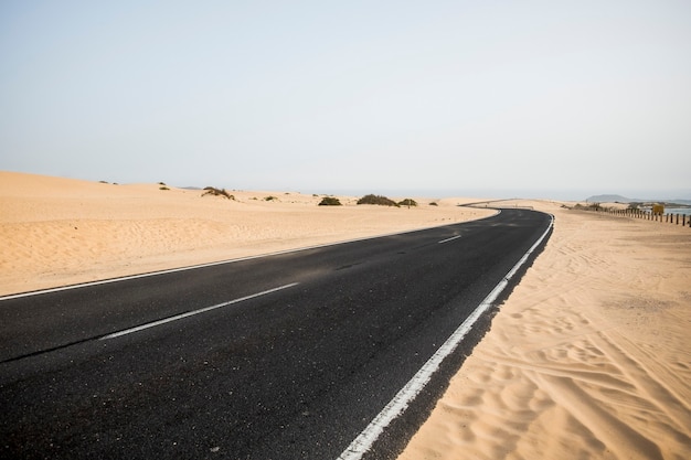 Schwarze Asphaltstraße in der Mitte der Wüste, die die Sanddünen im Naturparkgebiet fuerteventura corralejo kreuzt. Gefühl des Abenteuers mit niemandem dort. alternativer Ort für Tourismus oder Urlaub