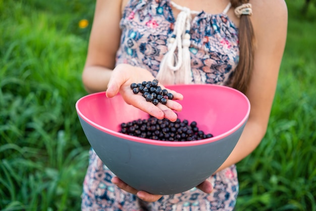 Schwarze Beeren von frischen Johannisbeeren in der Hand eines Mädchens in einem Sommerkleid im Freien