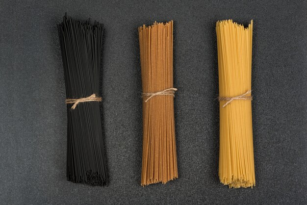 Schwarze, braune und gelbe Spaghetti auf grauem Raum. Italienische trockene Pasta. Spaghetti-Raum.