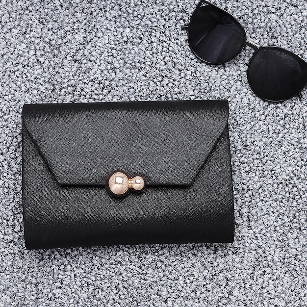 Schwarze Damen-Clutch mit Brille auf silbernem Hintergrund, Draufsicht