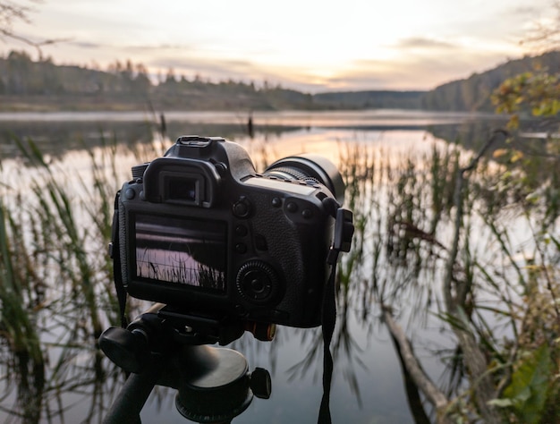 Foto schwarze digitalkamera auf stativ, die neblige landschaft am frühen morgen am herbstsee mit selektivem fokus aufnimmt