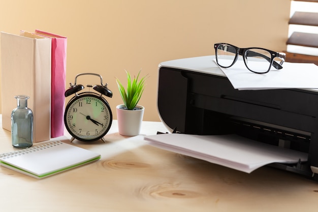 Schwarze Druckermaschine auf einem Tisch mit Wecker und Büchern