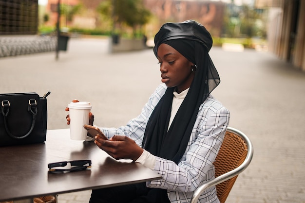 Schwarze elegante Frau trinkt Kaffee und surft auf dem Smartphone