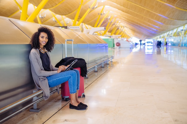 Schwarze Frau am Flughafen unter Verwendung der Tablette und der hörenden Musik mit Kopfhörern