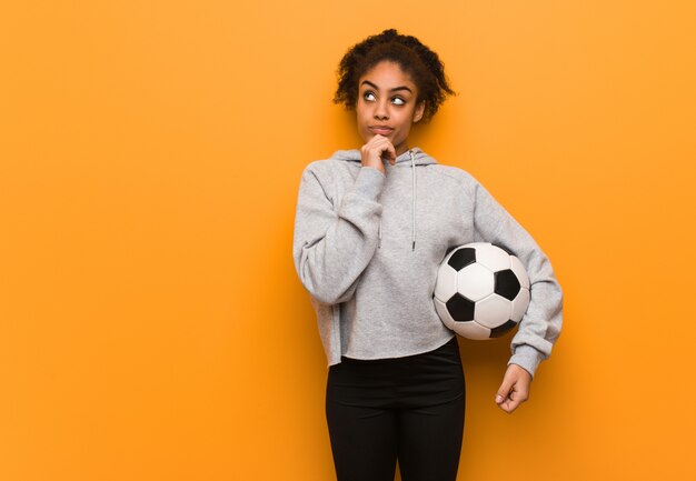 Schwarze Frau der jungen Eignung, die an eine Idee denkt. Einen Fußball halten.