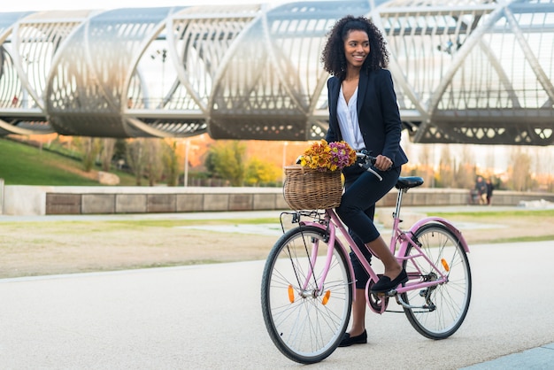 Schwarze Frau des Geschäfts, die Weinlesefahrrad in der Stadt fährt