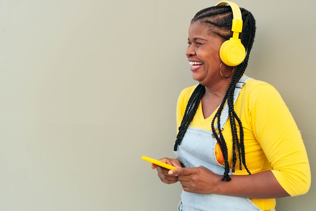 Schwarze Frau, die draußen Musik auf einem Smartphone hört.