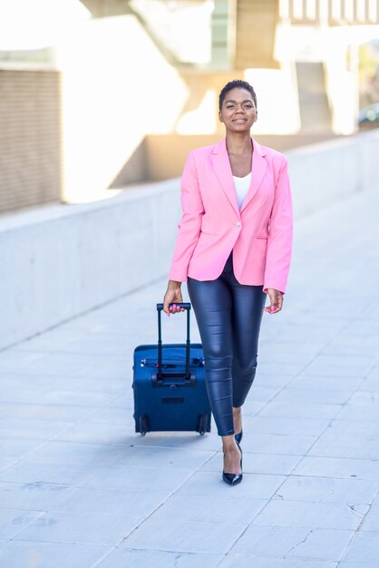 Schwarze frau, die mit der reisetasche trägt rosa jacke geht.