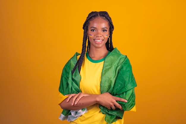 Schwarze Frau junger brasilianischer Fußballfan verschränkte die Arme selbstbewusst glücklich fröhlich Junge afro-brasilianische Cheerleaderin mit verschränkten Armen auf gelbem Hintergrund