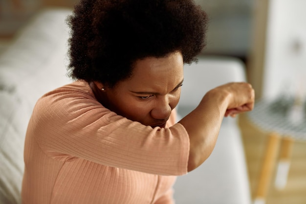 Schwarze Frau mit Grippevirus, die zu Hause in den Ellbogen niest