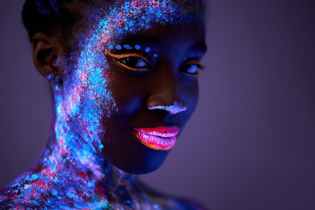 Schwarze Frau mit Körperkunst, die in ultraviolettem Licht leuchtet, schöne Frau, die in fluoreszierendem Puder gemalt ist ...