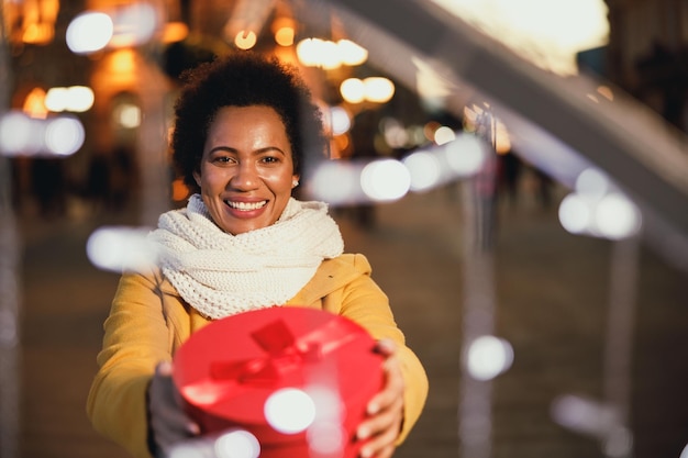 Schwarze Frau mittleren Alters, die in der festlichen Nacht der Stadt ein Geschenk auf dem Weihnachtsmarkt hält.